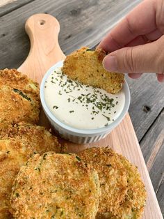 someone dipping some food into a small bowl on a cutting board with dip in it