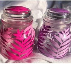 two glass jars with pink and purple leaves painted on the lids are sitting on a white sheet