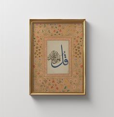 an arabic calligraphy is displayed in a gold frame on a white wall with floral designs