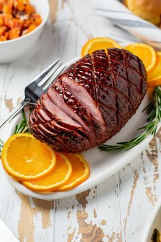 sliced ham on a plate with orange slices and rosemary garnish next to it