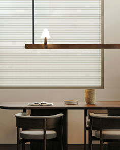 a table with two chairs and a book on it in front of a window that has blinds