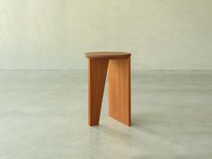 a small wooden stool sitting on top of a cement floor next to a white wall