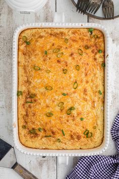 a casserole dish with cheese and green onions in it on a white wooden table