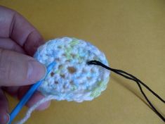 a crocheted flower being worked on by someone using a blue knitting needle to hold the yarn