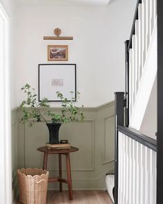 a plant in a black vase sitting on top of a wooden table next to a stair case