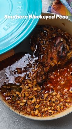 a pot filled with beans and meat on top of a table next to a blue plate