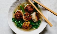 a white plate topped with meatballs and green vegetables next to chopsticks on top of a table