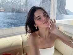 a woman sitting on top of a boat next to the ocean with her hands up