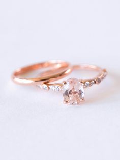 two gold wedding rings with an oval morganite and white diamonds on the side, set against a plain background