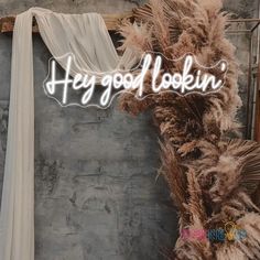 there is a sign that says hey good looking in front of a wall with feathers