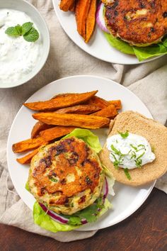 two plates with burgers and sweet potato wedges on them, along with ranch dressing