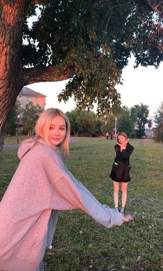 two women standing under a tree in a park, one holding the other's hand