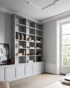 an empty living room with bookshelves and a television on the wall, in front of a large window