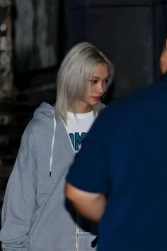 a woman with white hair is standing in front of a man wearing a blue shirt