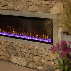 an electric fireplace with purple flame and rocks on the wall next to it, surrounded by flowers