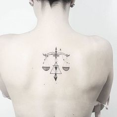 the back of a woman's neck with a scale and arrow tattoo on it