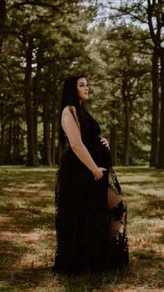 a pregnant woman standing in the woods wearing a black dress with sheer stockings and high heels