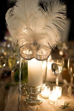 a candle and some white feathers on a table with candles in the centerpieces