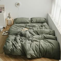 an unmade bed sitting on top of a hard wood floor next to a window