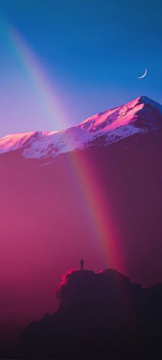 a man standing on top of a mountain under a rainbow