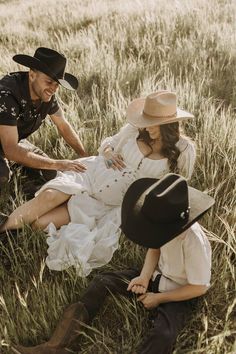 a man and woman sitting in the grass with cowboy hats on their heads, looking at each other