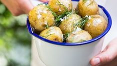 a person holding a blue and white bowl full of potatoes with dill sprig on top