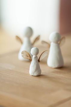 three small white angel figurines sitting on top of a wooden table next to each other