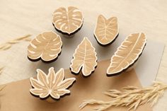 four wooden leaves are sitting on top of a piece of paper next to some dried grass