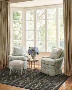 a living room with two chairs and a table in front of a large window filled with curtains