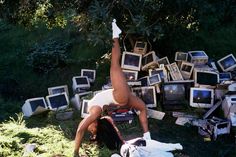 a woman standing on one leg in front of a pile of tvs and monitors