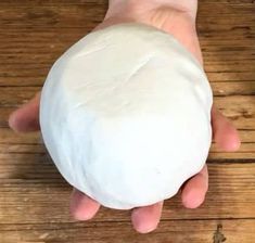 a person's hand holding a ball of dough on top of a wooden table