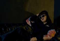 a woman sitting on top of a black leather couch wearing sunglasses and holding a fan