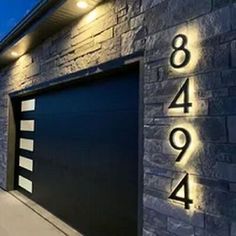 an illuminated house number sign on the side of a brick building with a garage door