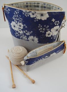 a blue and white flowered bag with two knitting needles in it next to a ball of yarn