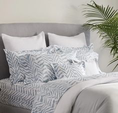 a bed with blue and white sheets and pillows on top of it next to a potted plant