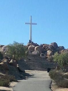 a cross on top of a hill with stairs leading up to it and trees in the foreground