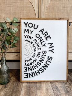 a framed art piece with the words you are my sunshine shine on it and a green vase next to it