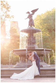 a bride and groom kissing in front of a fountain with an angel statue behind them