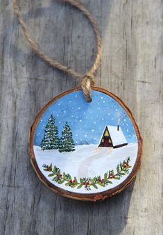 a wooden ornament with a cabin in the snow and pine trees on it