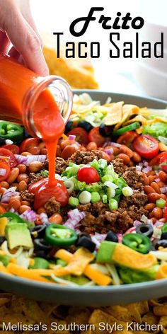 someone is pouring dressing into a plate of taco salad with tortilla chips