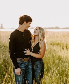 a young man and woman standing in tall grass looking into each other's eyes