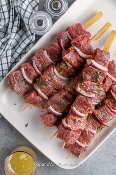 skewered meat and onions on a white plate with mustard next to the bowl