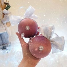 two red balls with bows are held in the air by someone's hand and snow is falling around them