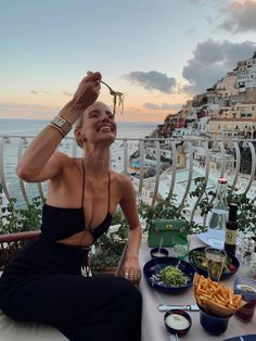 a woman sitting at a table with food in front of her and the ocean behind her