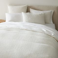 a bed with white linens and pillows on it's headboard, next to a wicker basket