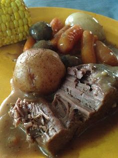 a yellow plate topped with meat and vegetables next to a corn on the cob