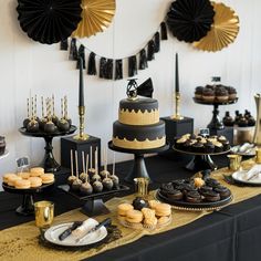 a table topped with cakes and desserts covered in black and gold decorations