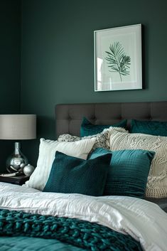 a bed with green and white pillows in a bedroom next to a framed painting on the wall