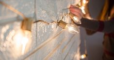 a person holding some lights next to a white brick wall with string lights on it