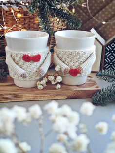 two knitted cups sitting on top of a wooden table next to a christmas tree